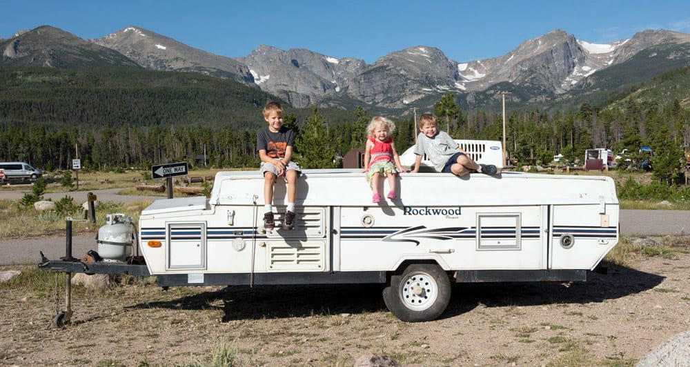 Three children sitting on RV pop-up trailer with mountains in background